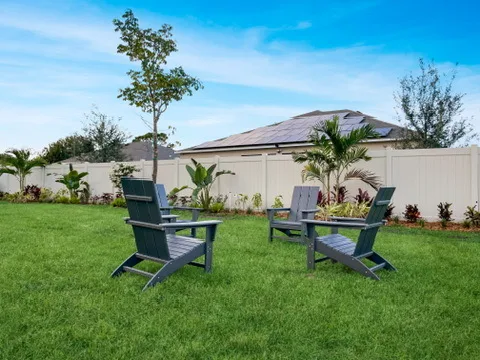 Large fenced backyard at Blue Breeze with Adirondack chairs and tropical landscaping