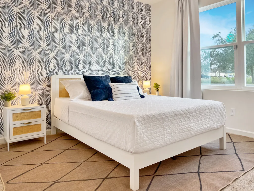 Bright bedroom at Blue Breeze with navy palm-frond wallpaper, a plush bed, and large sunny windows
