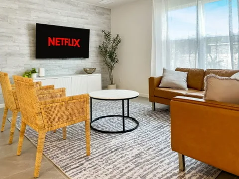 Open living room at Blue Breeze with a leather sofa, woven accent chairs, and a wall-mounted TV